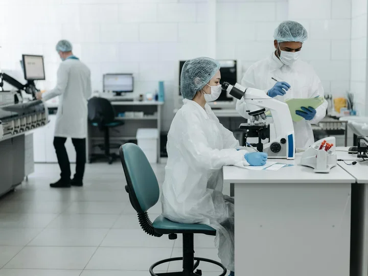 Three researchers in a lab looking at microscope and computer screens.
